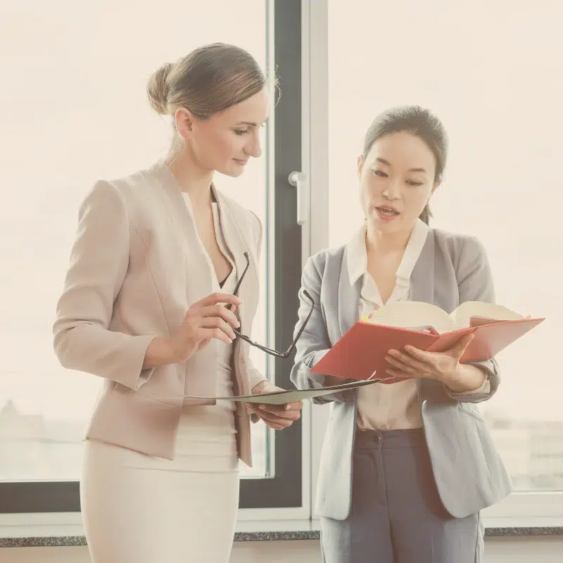 20+ Years of Experience Simple Law TX in Friendswood Texas two women reviewing the pages of a book together while standing and conversing about the book